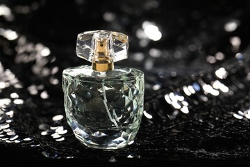 Luxury perfume in bottle on fabric with shiny sequins, closeup