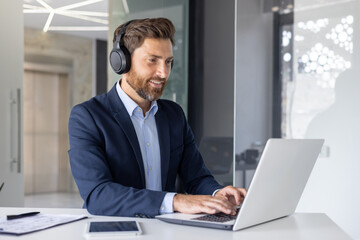 Smiling businessman with headphones using laptop in office