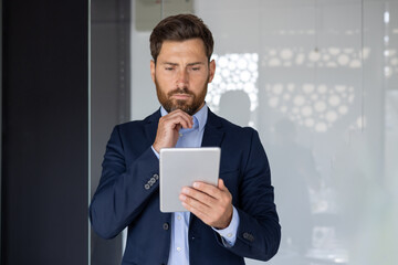 Serious businessman thinking while holding tablet in office