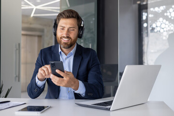 Smiling businessman using smartphone with headphones in office