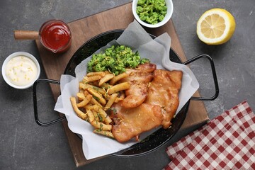 Tasty fish, chips, sauces and peas on grey table, flat lay