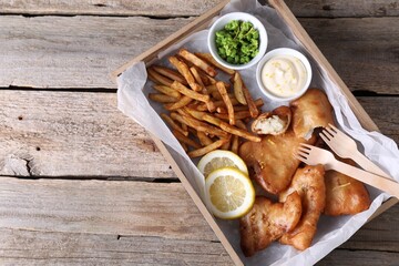 Tasty fish, chips, sauce and peas on wooden table, top view. Space for text