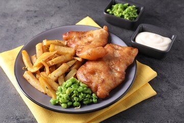 Tasty fish, chips, sauce and peas on grey table, closeup