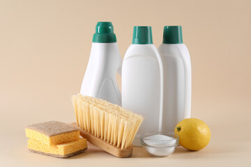 Bottles of cleaning product, sponges, brush, lemon and baking soda on beige background