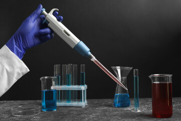 Laboratory analysis. Scientist holding micropipette with liquid at grey table, closeup
