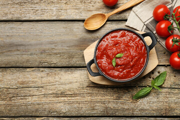 Homemade tomato sauce in bowl, spoon and fresh ingredients on wooden table, flat lay. Space for text
