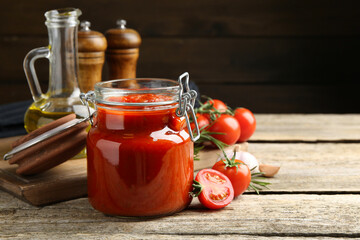 Homemade tomato sauce in jar and ingredients on wooden table, closeup. Space for text