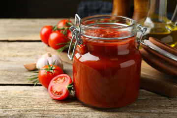Homemade tomato sauce in jar and fresh ingredients on wooden table, closeup