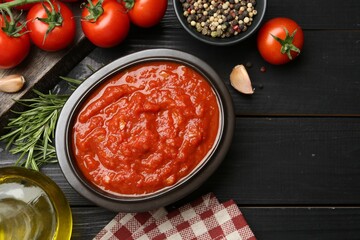 Homemade tomato sauce in bowl and fresh ingredients on black wooden table, flat lay