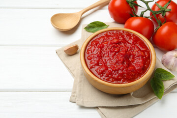 Homemade tomato sauce in bowl, spoon and fresh ingredients on white wooden table. Space for text
