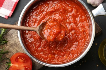 Homemade tomato sauce and spoon in pot on dark table, flat lay