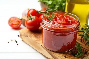 Homemade tomato sauce in jar and fresh ingredients on white wooden table, closeup