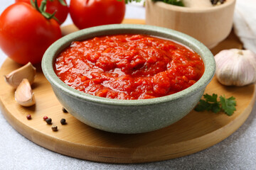 Homemade tomato sauce in bowl and fresh ingredients on light grey table, closeup