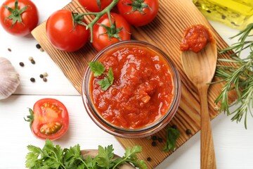 Homemade tomato sauce in jar, spoon and fresh ingredients on white wooden table, flat lay