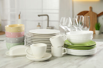 Clean plates, bowls, cups and glasses on white marble table in kitchen