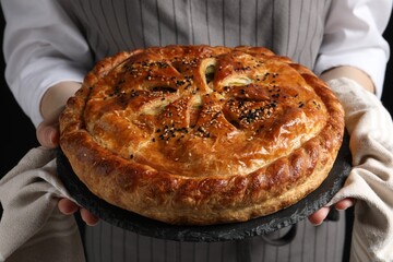 Woman holding tasty homemade pie on black background, closeup