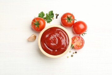 Delicious ketchup in bowl, peppercorns and tomatoes on white wooden table, flat lay