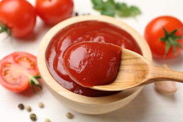 Taking delicious tomato ketchup with spoon from bowl at white table, closeup