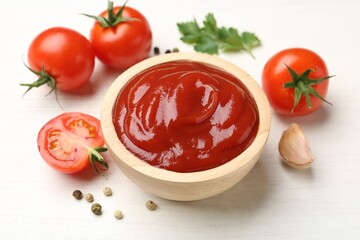 Delicious ketchup in bowl, garlic and tomatoes on white wooden table, closeup