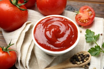 Delicious ketchup in bowl, tomatoes, parsley and peppercorns on table, closeup