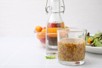 Tasty vinegar based sauce (Vinaigrette) in glass on light tiled table, closeup. Space for text