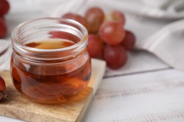 Wine vinegar in glass jar and grapes on light wooden table, closeup. Space for text