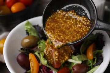 Pouring tasty vinegar based sauce (Vinaigrette) into bowl with salad, closeup