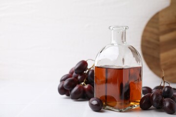 Wine vinegar in glass bottle and grapes on white table, space for text