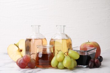 Different types of vinegar and ingredients on light marble table, closeup
