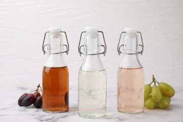 Different types of vinegar in bottles and grapes on light marble table, closeup
