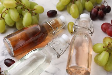 Different types of vinegar in bottles and grapes on light table, closeup