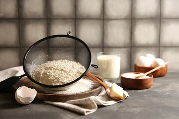 Making dough. Flour in sieve, spoon and butter on grey table, closeup