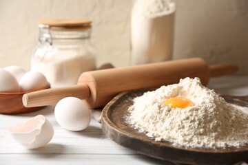 Making dough. Pile of flour with yolk, rolling pin and eggs on white wooden table, closeup