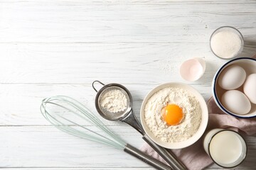 Flour with yolk in bowl and other ingredients for dough on white wooden table, flat lay. Space for text