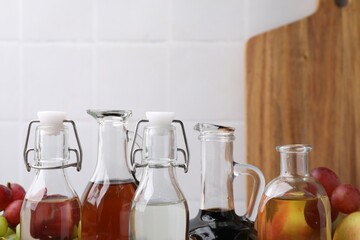 Different types of vinegar and fresh fruits against blurred background