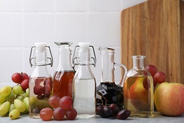 Different types of vinegar and fresh fruits on grey table