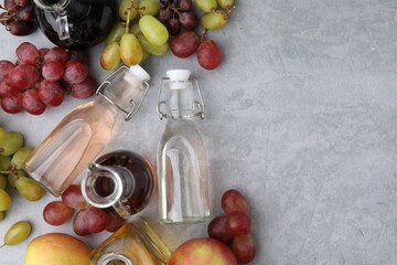 Different types of vinegar and fresh fruits on grey table, flat lay. Space for text