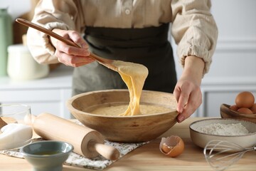 Woman kneading dough with spoon in bowl at wooden table in kitchen, closeup