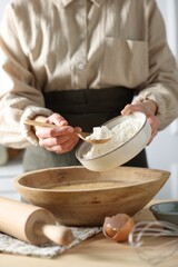 Making dough. Woman adding flour into bowl at wooden table in kitchen, closeup