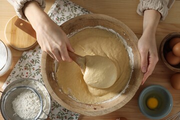 Woman kneading dough with spoon in bowl at wooden table, top view