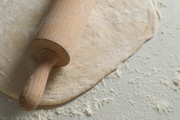 Raw dough and rolling pin on table, closeup