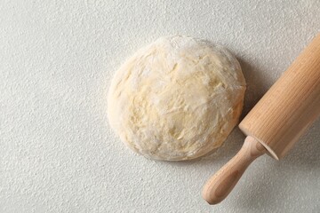 Raw dough and rolling pin on white table, top view. Space for text