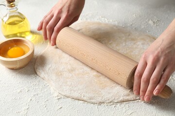 Woman rolling raw dough at table, closeup