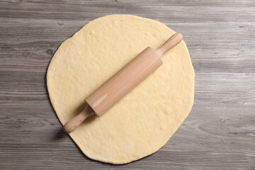 Raw dough and rolling pin on wooden table, top view