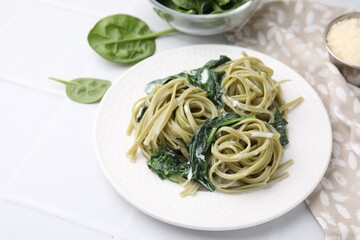 Tasty pasta with spinach and sauce on white tiled table