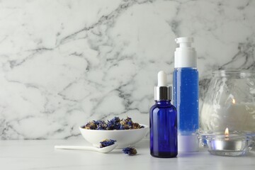 Spa composition. Bottles of cosmetic products, dry flowers and burning candles on white marble table, space for text