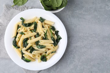 Tasty pasta with spinach and sauce on grey textured table, top view. Space for text