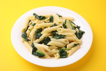 Tasty pasta with spinach and sauce on yellow table