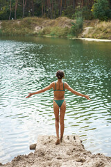 Fototapeta premium Back view of woman in bikini with perfect tan body enjoys the tranquil lake , opening arms