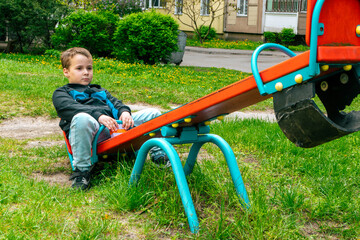 Sad little boy sits alone on a swing. The child is bored on the playground